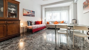 A modern living room with a sofa, a dining table with chairs, a cabinet, and a painting on the wall. - Livia's Vatican House - Metro Aurelia (Rome)