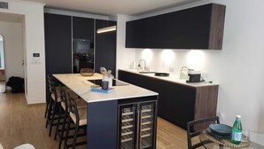 A modern kitchen with a central island, dark cabinetry, and a built-in wine cooler. - Villa Candide A409 by Avecoeur - Bail mobilité uniquement (Nice)