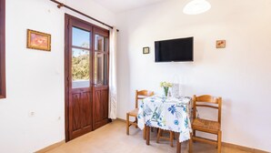 Zona de menjador amb una taula preparada per a dues persones, un televisor penjat a la paret i una porta de fusta amb una finestra.
