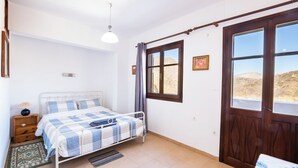 Un dormitori amb un llit, una tauleta de nit, una finestra amb vistes i una porta.