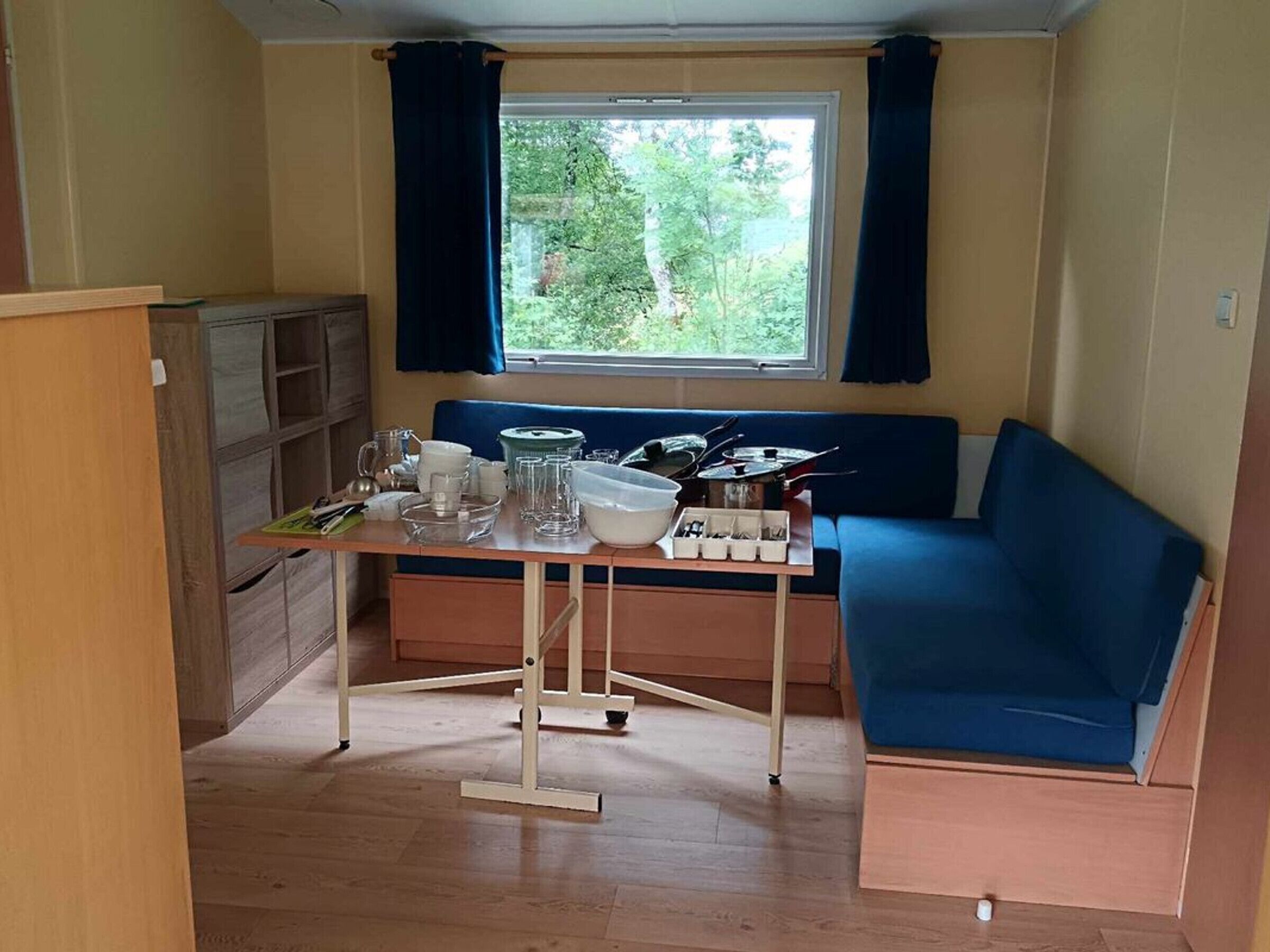 Pieni huone, jossa on pieni keittiö, ruokapöytä, sininen sohva ja ikkuna, jossa on verhot.