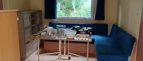 Pieni huone, jossa on pieni keittiö, ruokapöytä, sininen sohva ja ikkuna, jossa on verhot.
