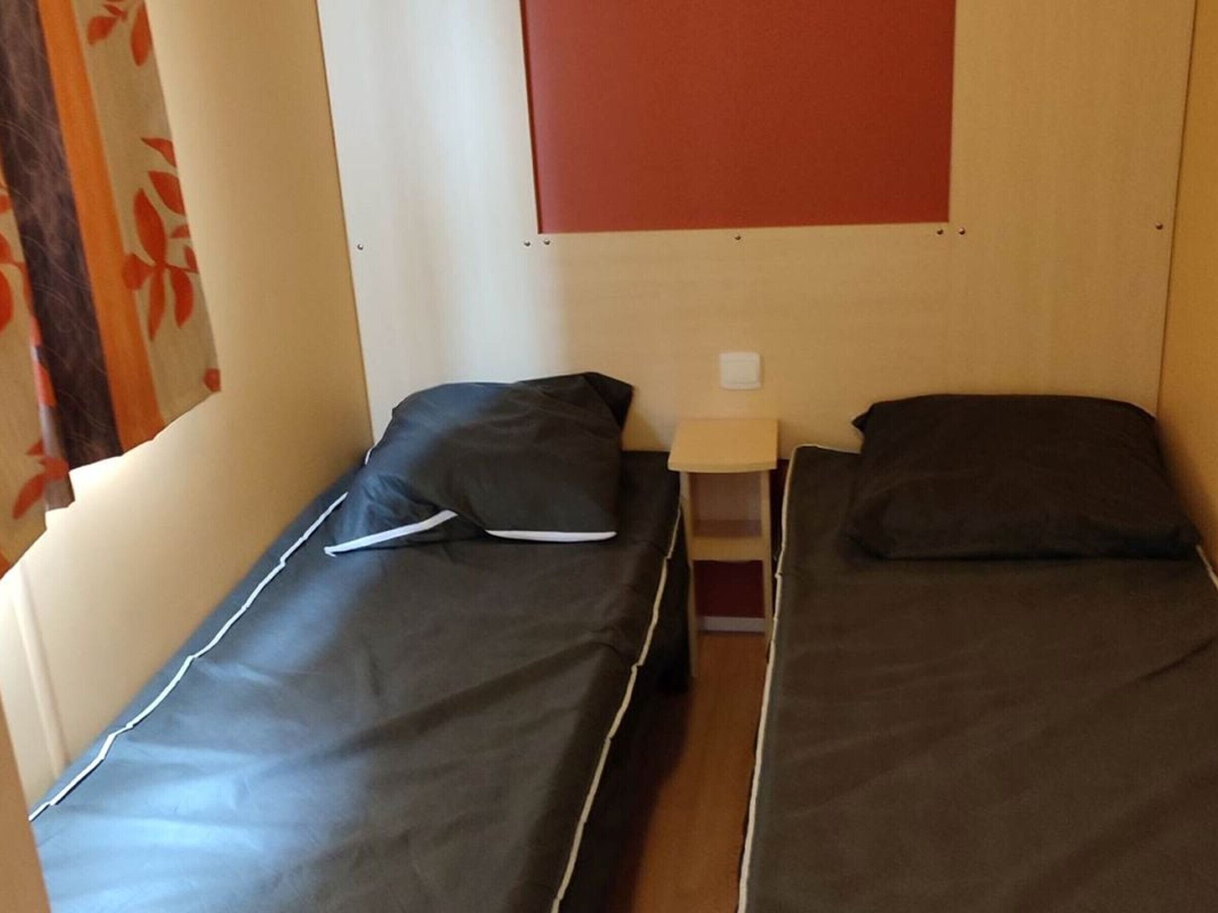 A small room with two beds, a nightstand, and a wall-mounted light.