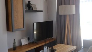 Ein Hotelzimmer mit Flachbildfernseher, einem Holztisch, einer Lampe und einem Regal mit Dekoration.