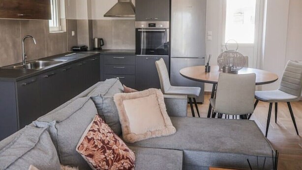Eine moderne Küche mit Essbereich, grauem Sofa und Stühlen.
