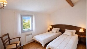 Ein Schlafzimmer mit zwei Betten, einem Fenster mit Blick, einem Sessel und einem Holzbalken an der Decke.