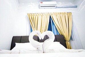 Une chambre d’hôtel avec un lit, des serviettes blanches, une décoration en forme de cœur réalisée avec des serviettes, un climatiseur fixé au mur et des rideaux.