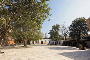 A courtyard with a large tree, a building with a dome, and a truck parked in the distance.