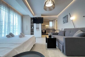 Une chambre d’hôtel moderne équipée d’un lit, d’un canapé, d’un téléviseur à écran plat, d’un coin cuisine et d’une table à manger.