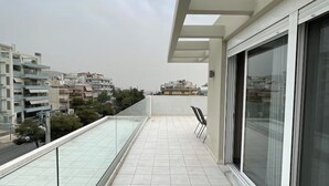 Un balcon doté d’une balustrade en verre, d’une chaise et offrant une vue sur les bâtiments environnants.