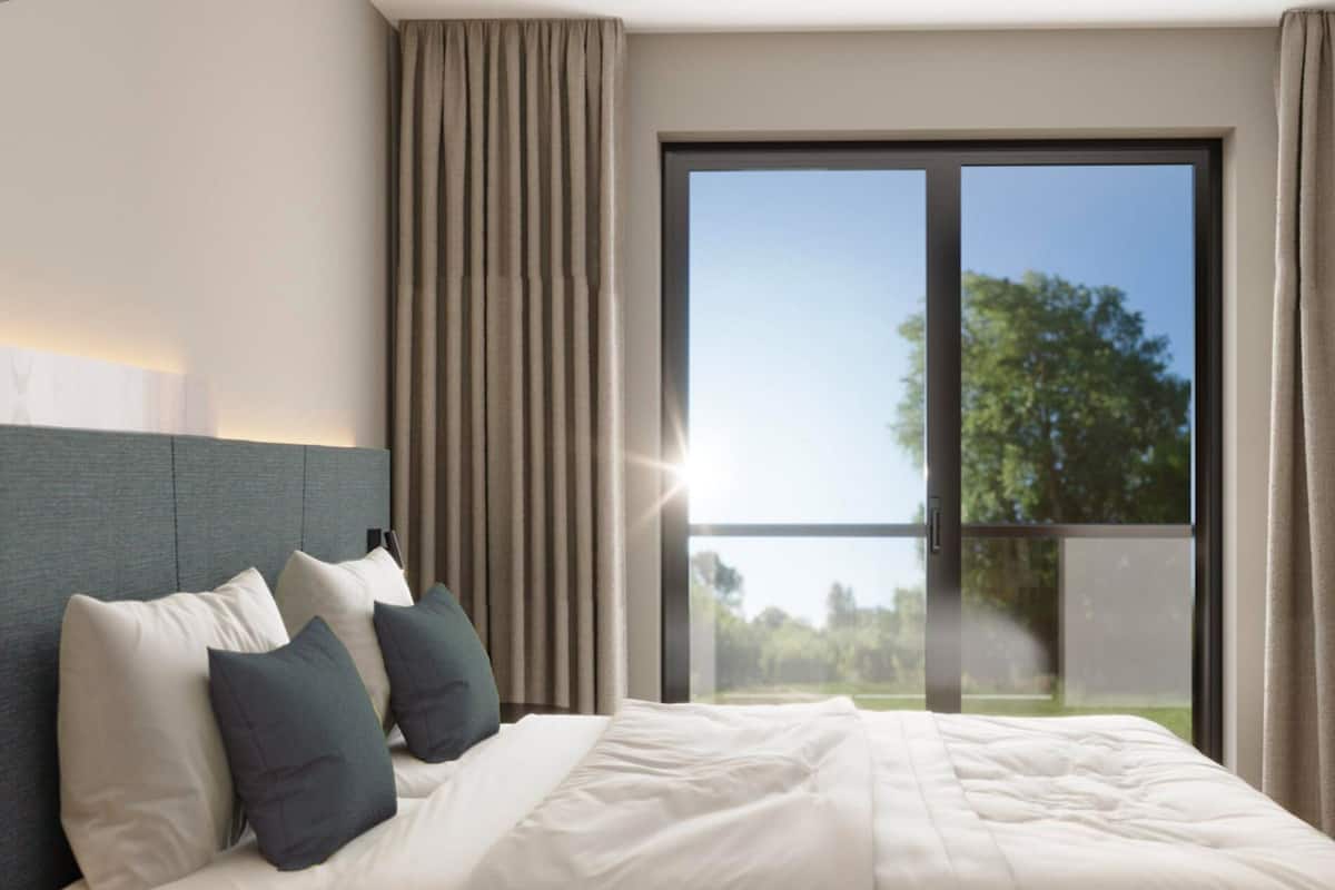 Una habitación de hotel con una cama grande, cabecera y ventana con cortinas.