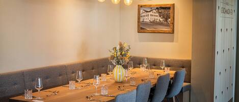 A dining area with a long table set for a meal, a vase with flowers, and a framed picture on the wall.