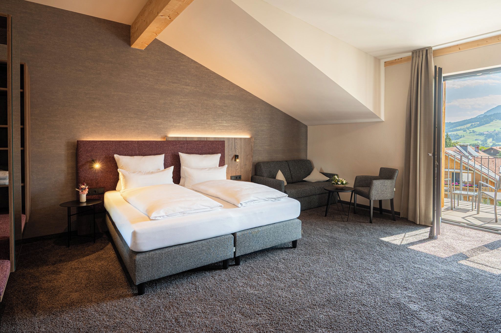 Une chambre d’hôtel moderne avec un grand lit, un canapé, une petite table et une vue sur la campagne.