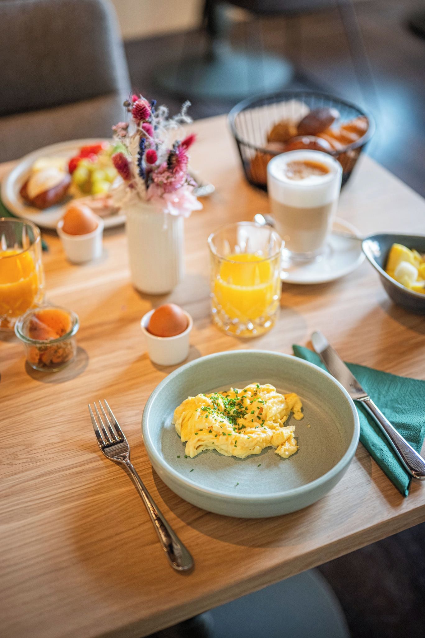 Une table en bois dressée pour le petit-déjeuner, avec des œufs brouillés, un verre de jus d’orange et une tasse de café.