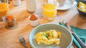 Une table en bois dressée pour le petit-déjeuner, avec des œufs brouillés, un verre de jus d’orange et une tasse de café.