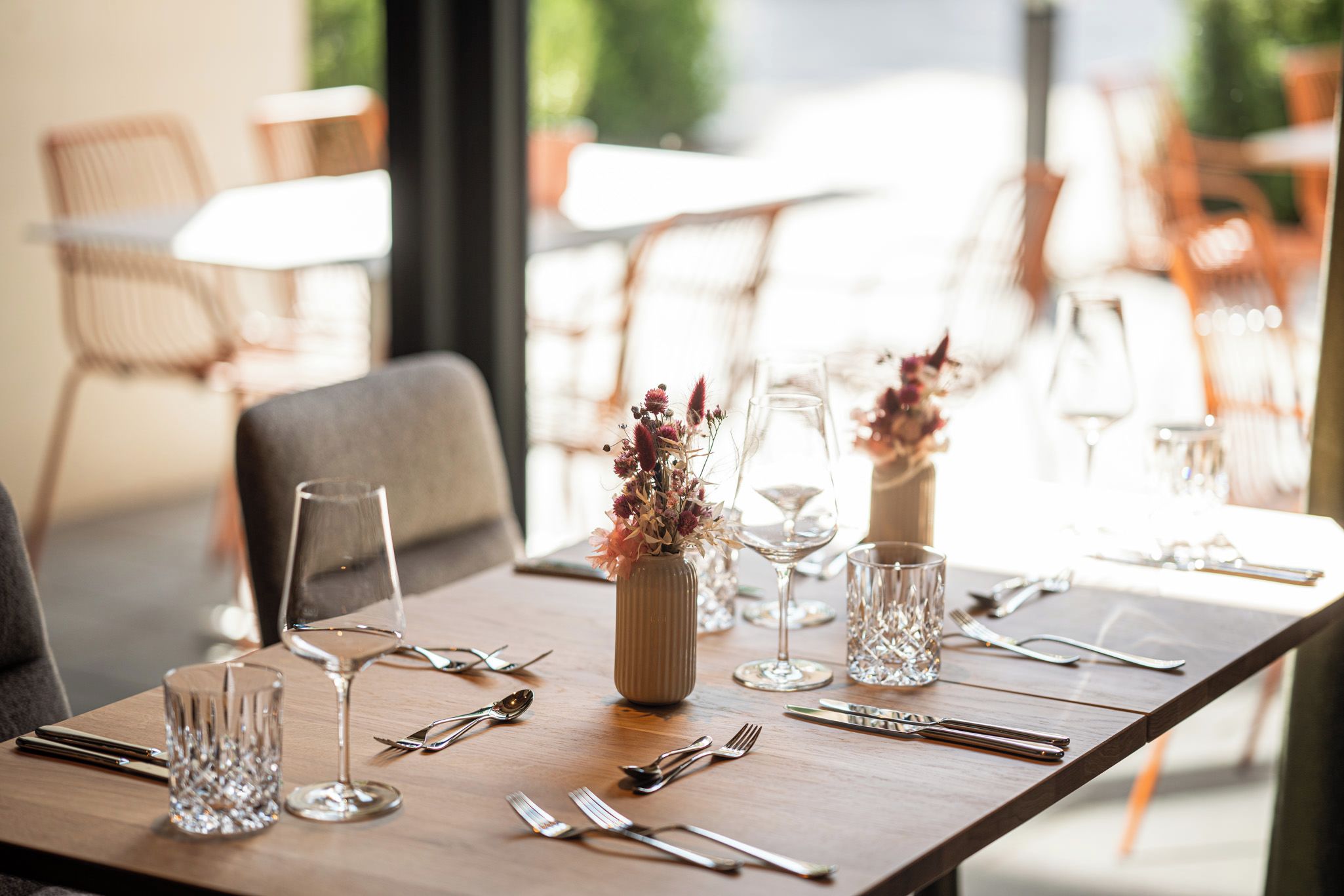 A dining table set with cutlery, glasses, and a vase with dried flowers.