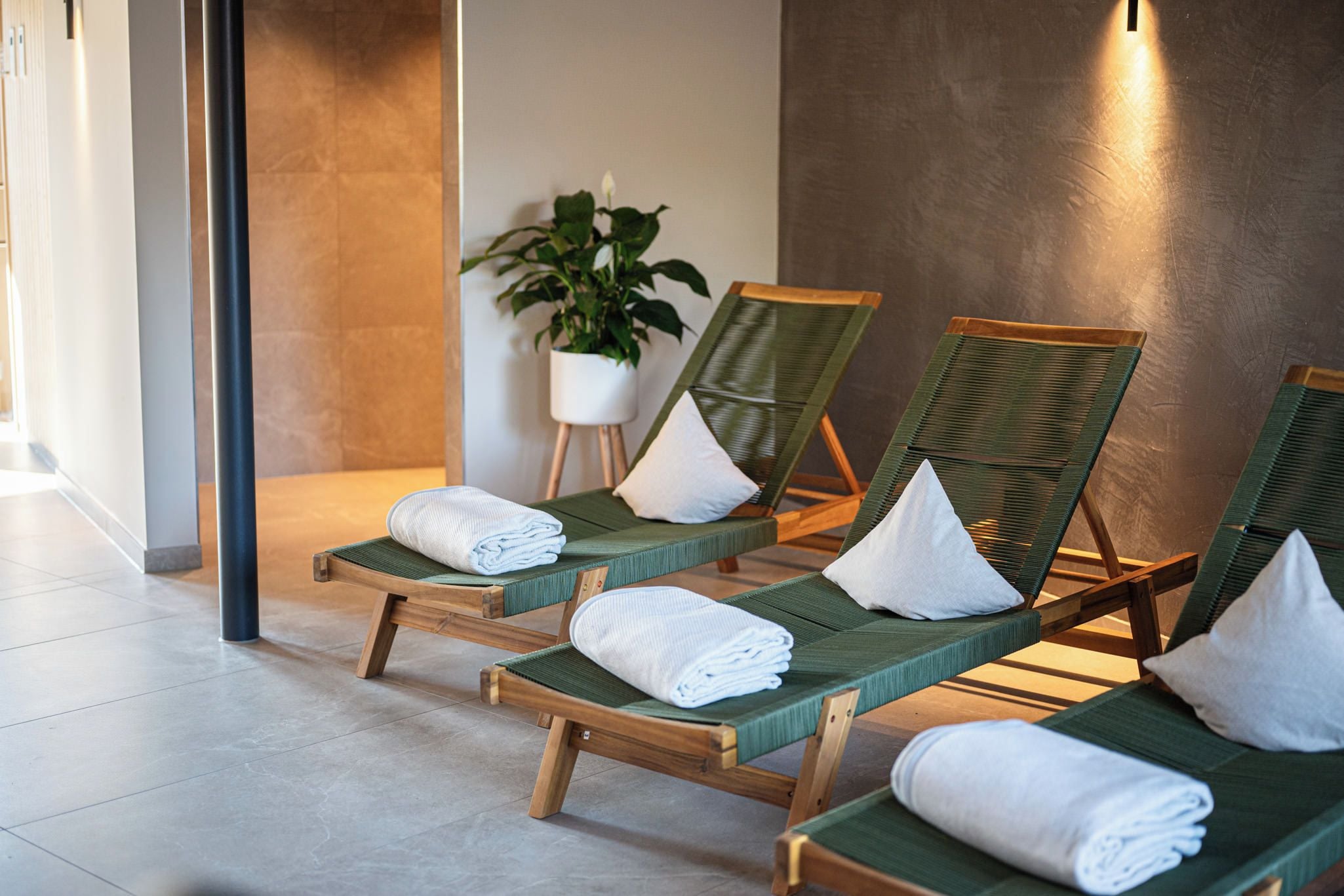 Un espace détente avec des chaises longues en bois, des serviettes blanches et une plante en pot.