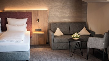 Ein Hotelzimmer mit einem Bett, einer Couch, einem Sessel, einem kleinen Tisch mit Blumen und einer Wandleuchte.