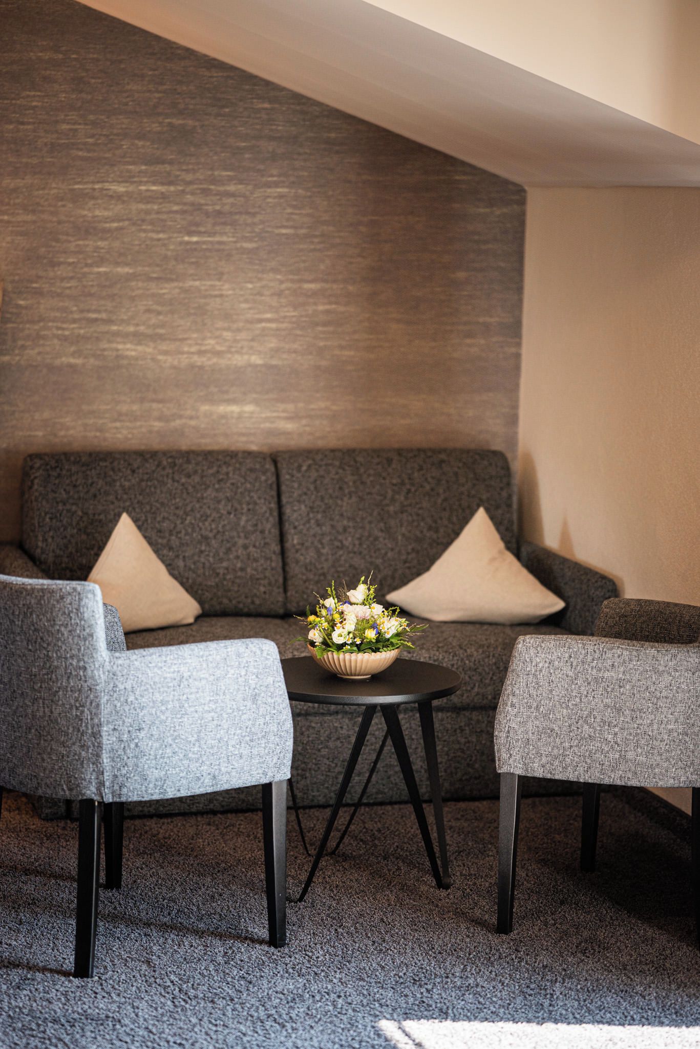 Un salon moderne avec un canapé gris, deux fauteuils, une petite table ronde et un arrangement floral.