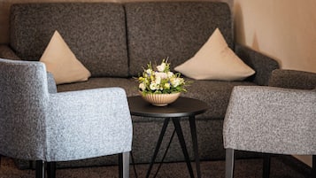 Un salon moderne avec un canapé gris, deux fauteuils, une petite table ronde et un arrangement floral.