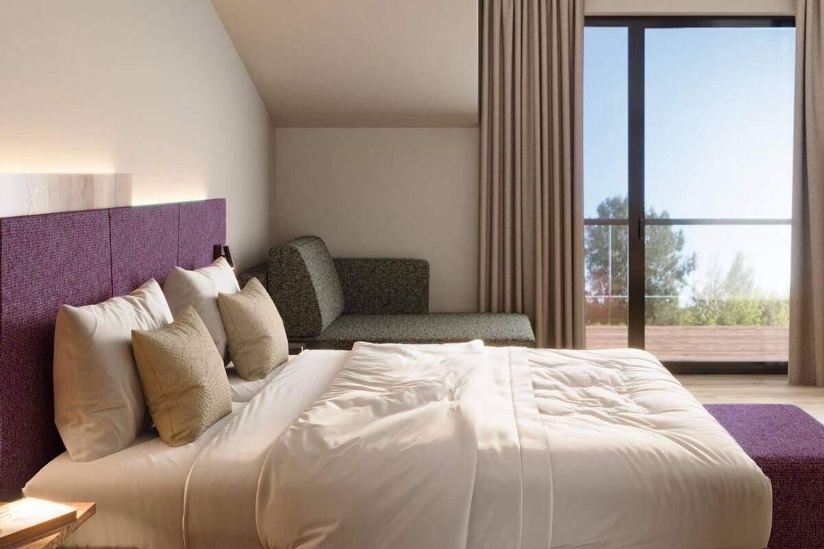 Habitación de hotel con una cama grande, un sofá, un balcón con cortinas y vistas al exterior.