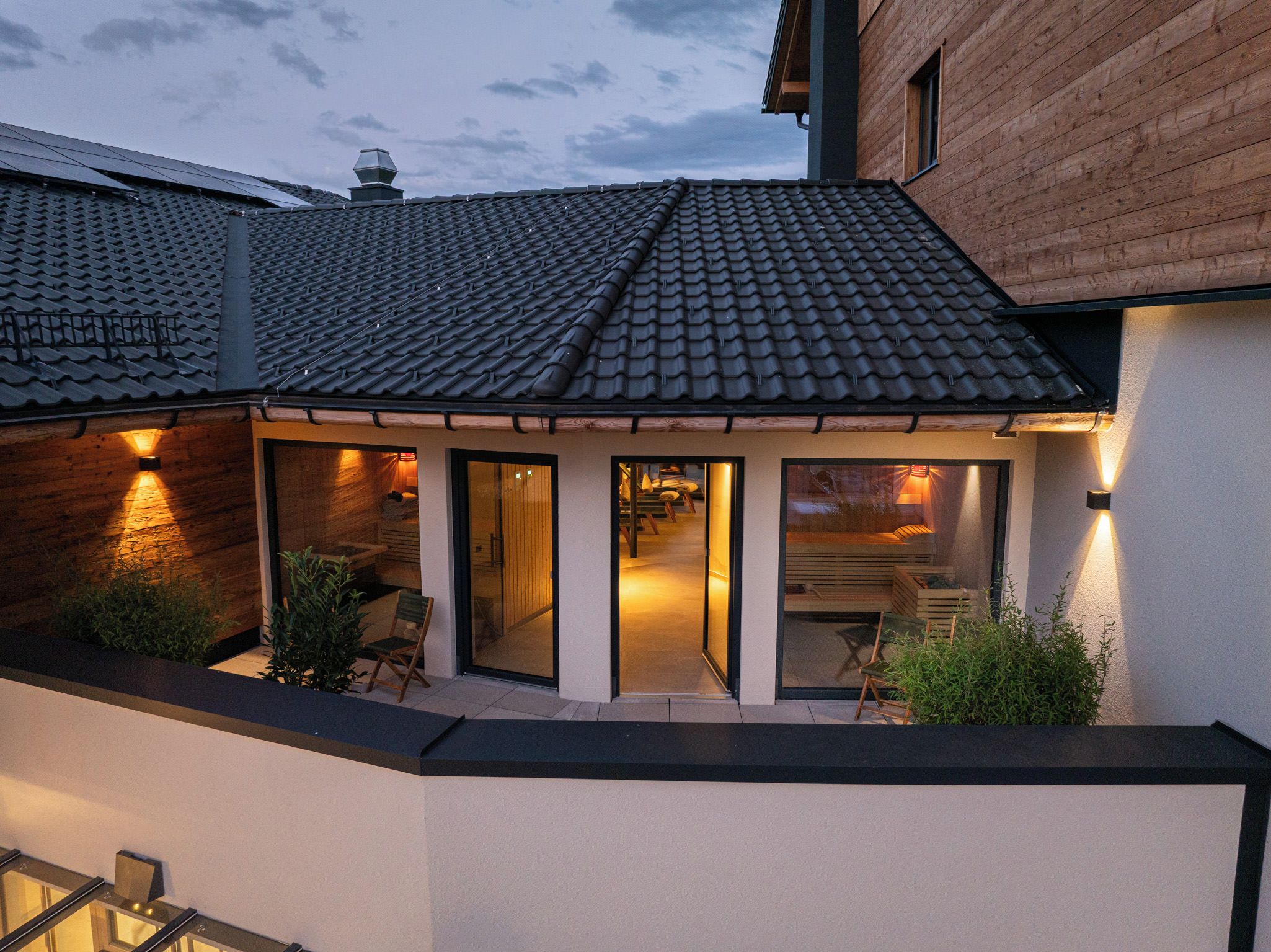 Una casa moderna con techo de tejas, un porche cubierto con sillas y un muro exterior de madera.