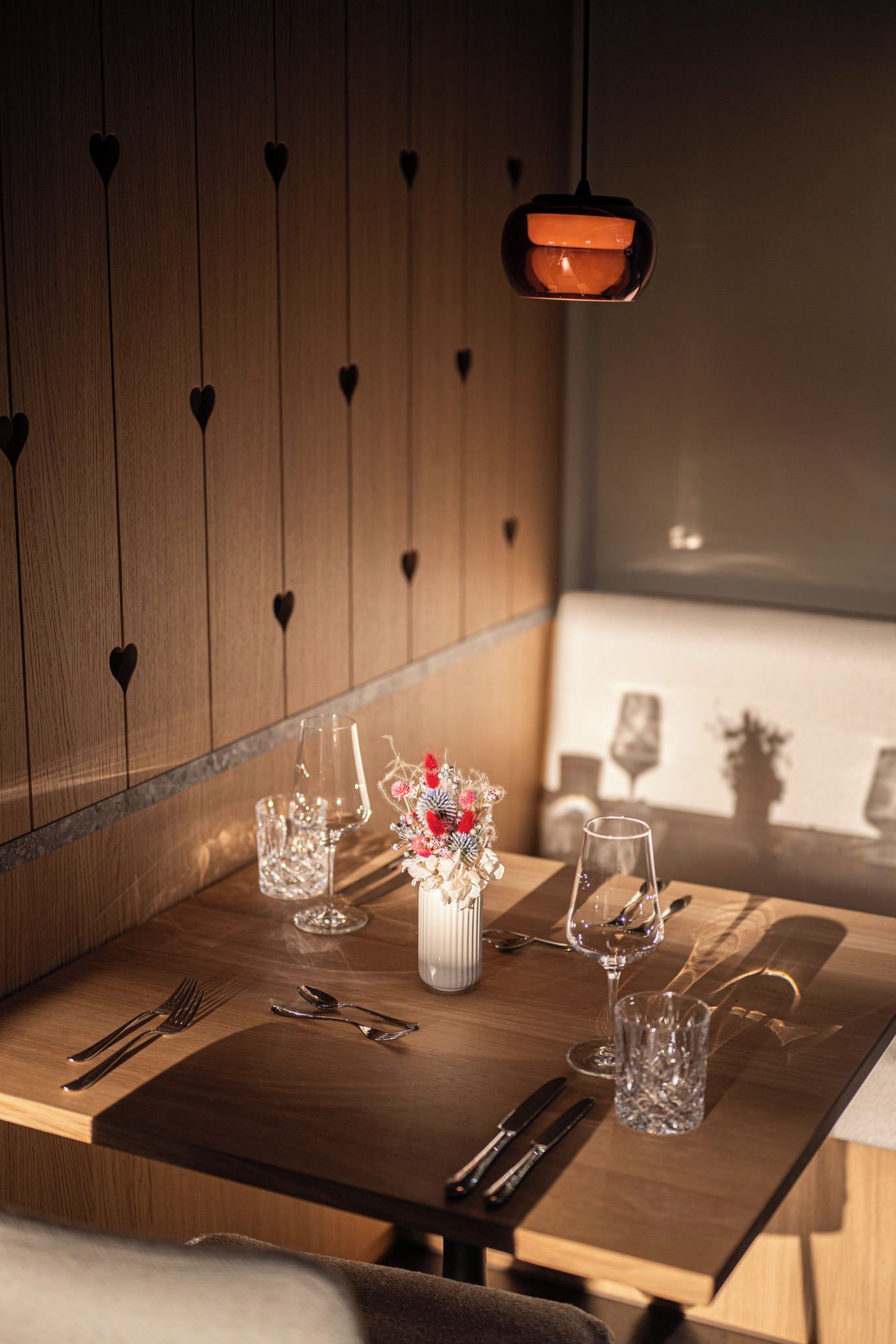 A dining table with a vase of flowers, cutlery, and wine glasses.
