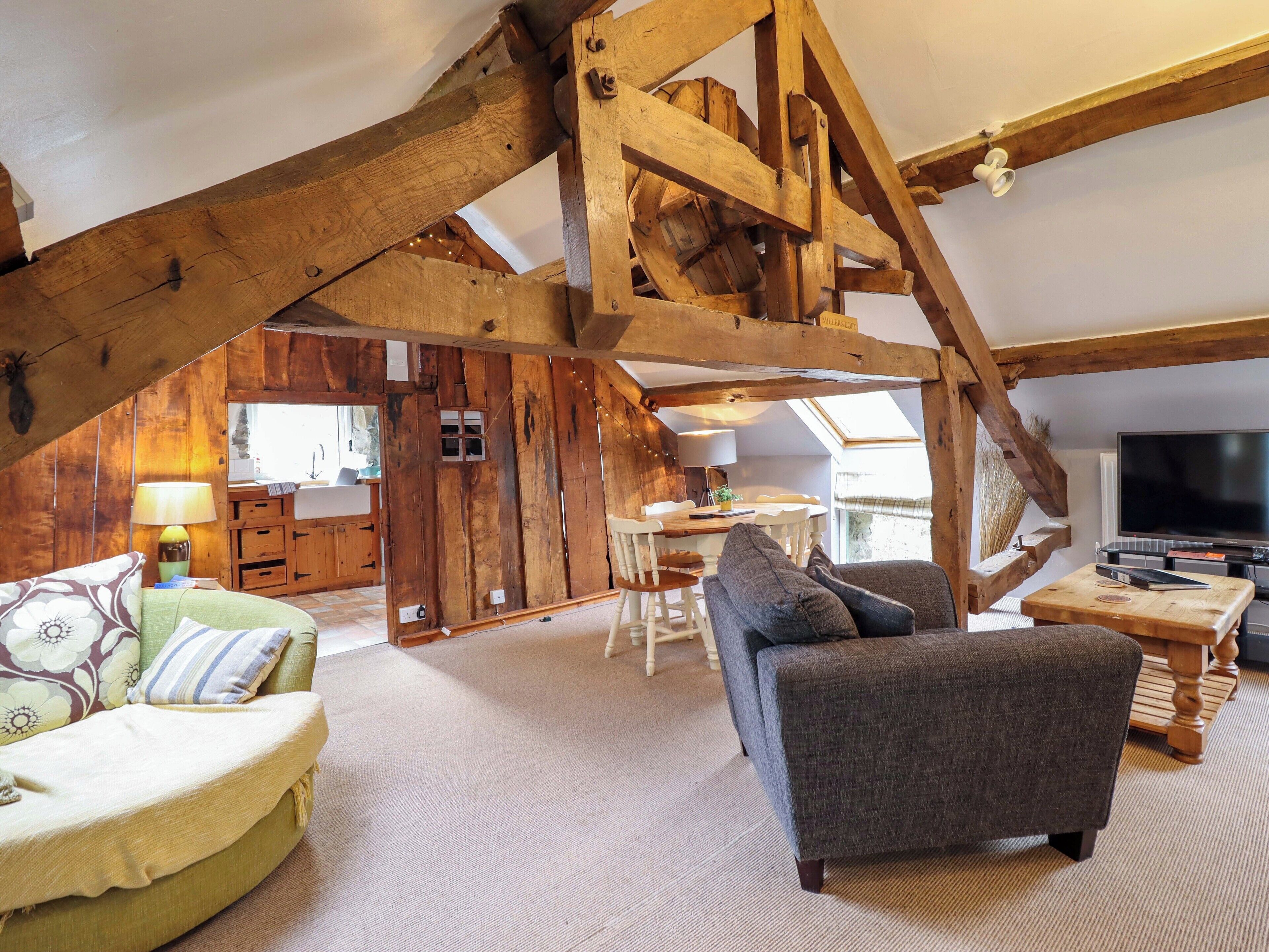 A rustic interior with exposed wooden beams, a sofa, a dining table, and a television.