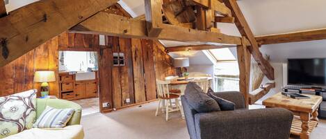 A rustic interior with exposed wooden beams, a sofa, a dining table, and a television.