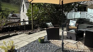 An outdoor patio with wicker furniture, a pergola, and a stone building in the background. - Millers Loft (Llanrwst)
