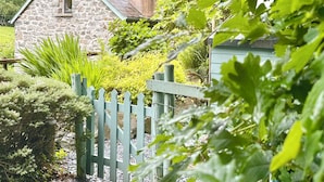 A stone cottage with a wooden fence, surrounded by lush greenery and a clear sky. - Millers Loft (Llanrwst)