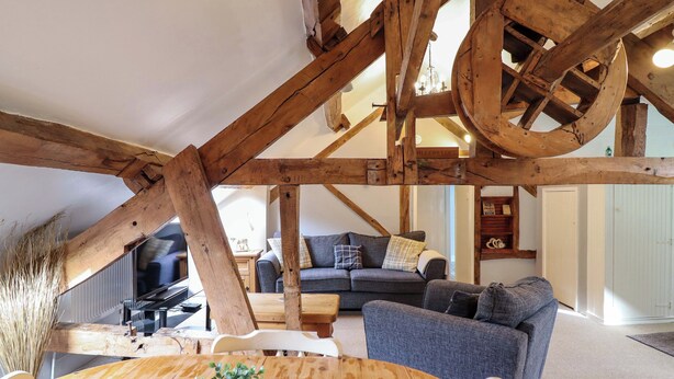 A rustic loft with exposed wooden beams, a round wooden table with a plant, a sofa, and a chair. - Millers Loft (Llanrwst)