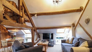 A rustic interior with exposed wooden beams, a sofa, a chair, a table, and a television. - Millers Loft (Llanrwst)