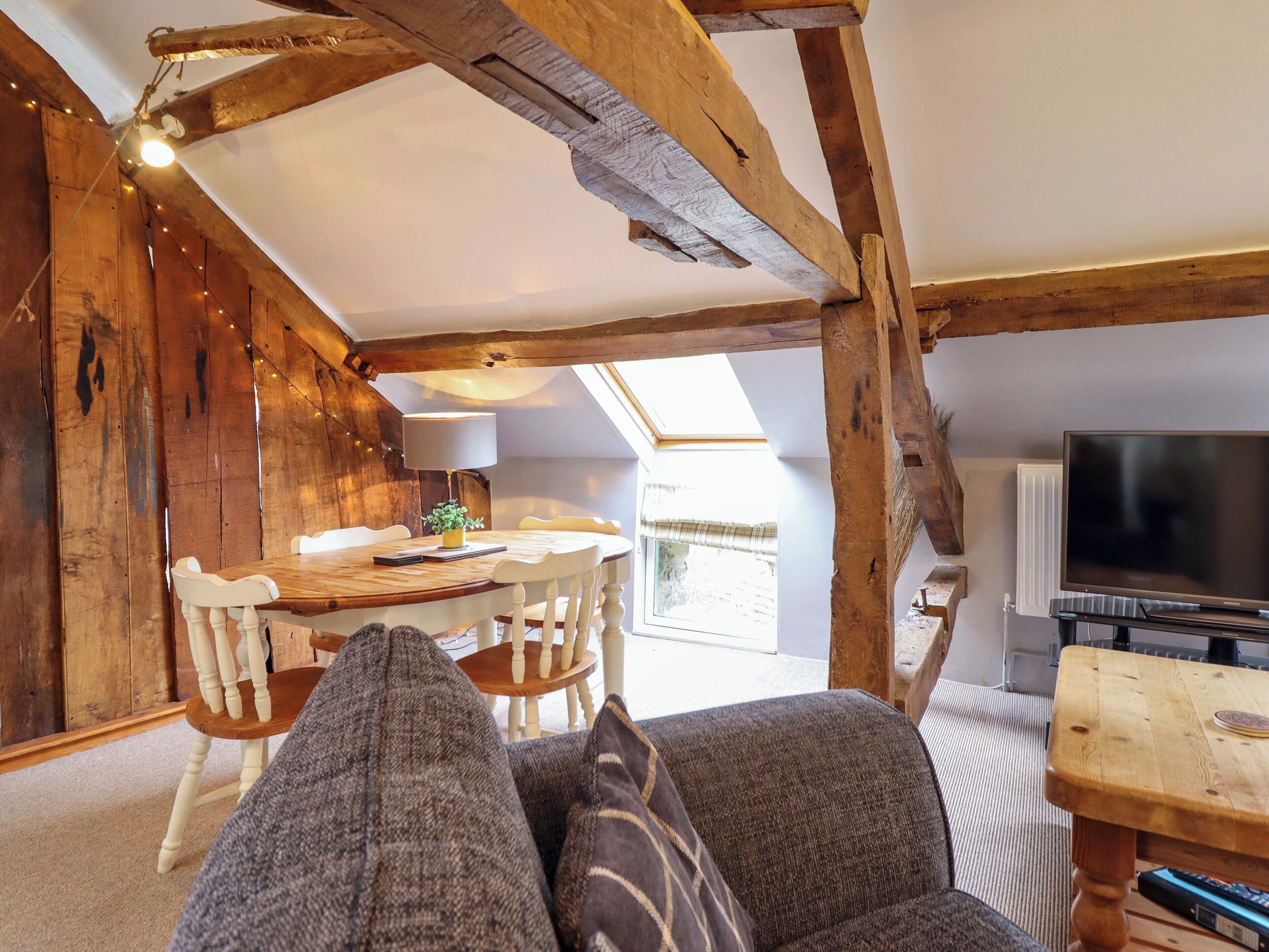 Una camera accogliente in stile loft, con travi a vista in legno, un tavolo da pranzo con sedie, un divano, una televisione e un lucernario.