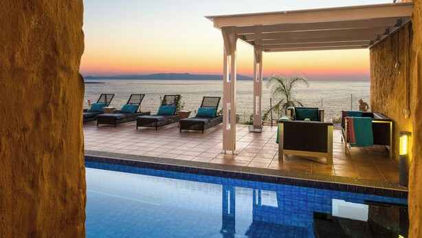 A poolside area with lounge chairs and a view of the sea at sunset. - Villas Maya 3-bedroom villa in fabulous Chorafakia with private pool (Chorafakia)
