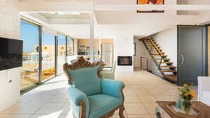 A spacious living area with a large window, a blue armchair, a staircase, and a flat-screen TV. - Villas Maya 3-bedroom villa in fabulous Chorafakia with private pool (Chorafakia)