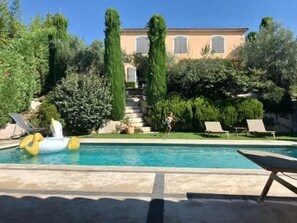 Ein Schwimmbad mit Liegestühlen, ein Haus mit Ziegeldach und ein gepflegter Garten.