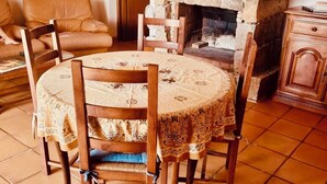 A cozy living room with a round wooden table, four chairs, a fireplace, a sofa, and a cabinet.
