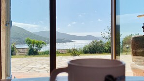 A view through a window with a white mug labeled 'Corsica' on a table.