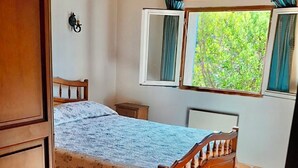 A bedroom with a wooden bed, a nightstand, a window with curtains, and a wall-mounted lamp.