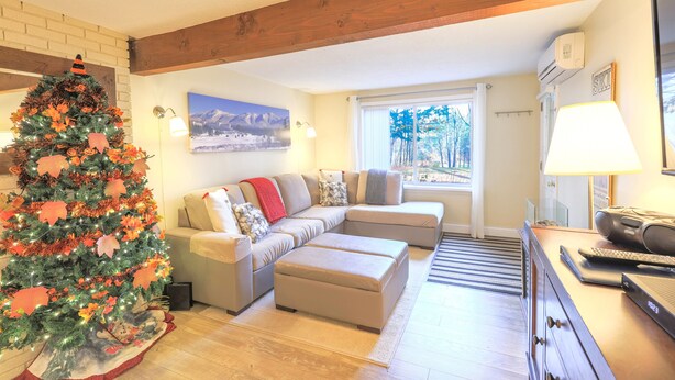 Una sala acogedora con un árbol de Navidad, un sofá seccional, una chimenea y un ventanal con vistas.
