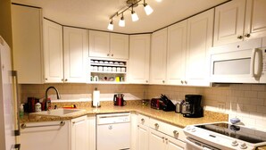 Una cocina con gabinetes blancos, lavavajillas, estufa y microondas.