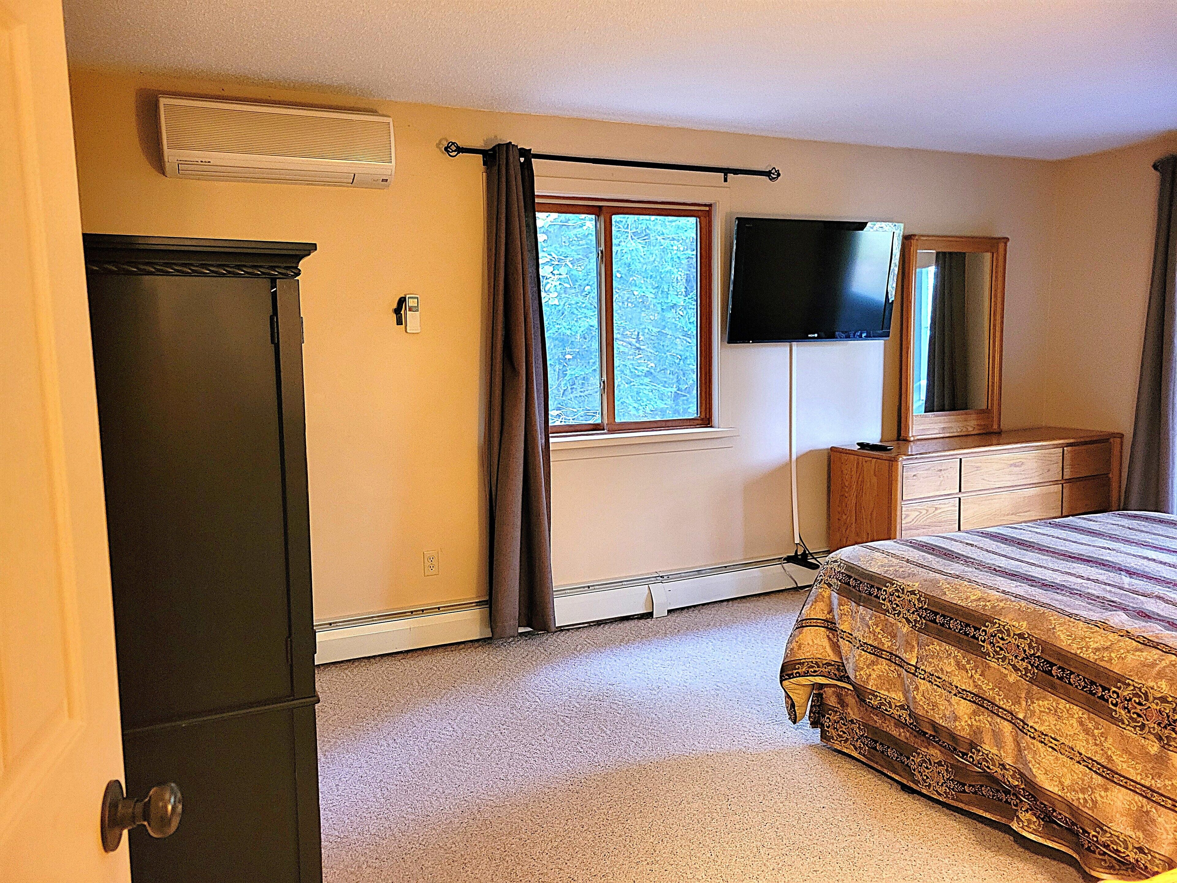 A bedroom with a bed, dresser, mirror, window, and air conditioning unit.