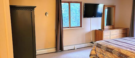 A bedroom with a bed, dresser, mirror, window, and air conditioning unit.