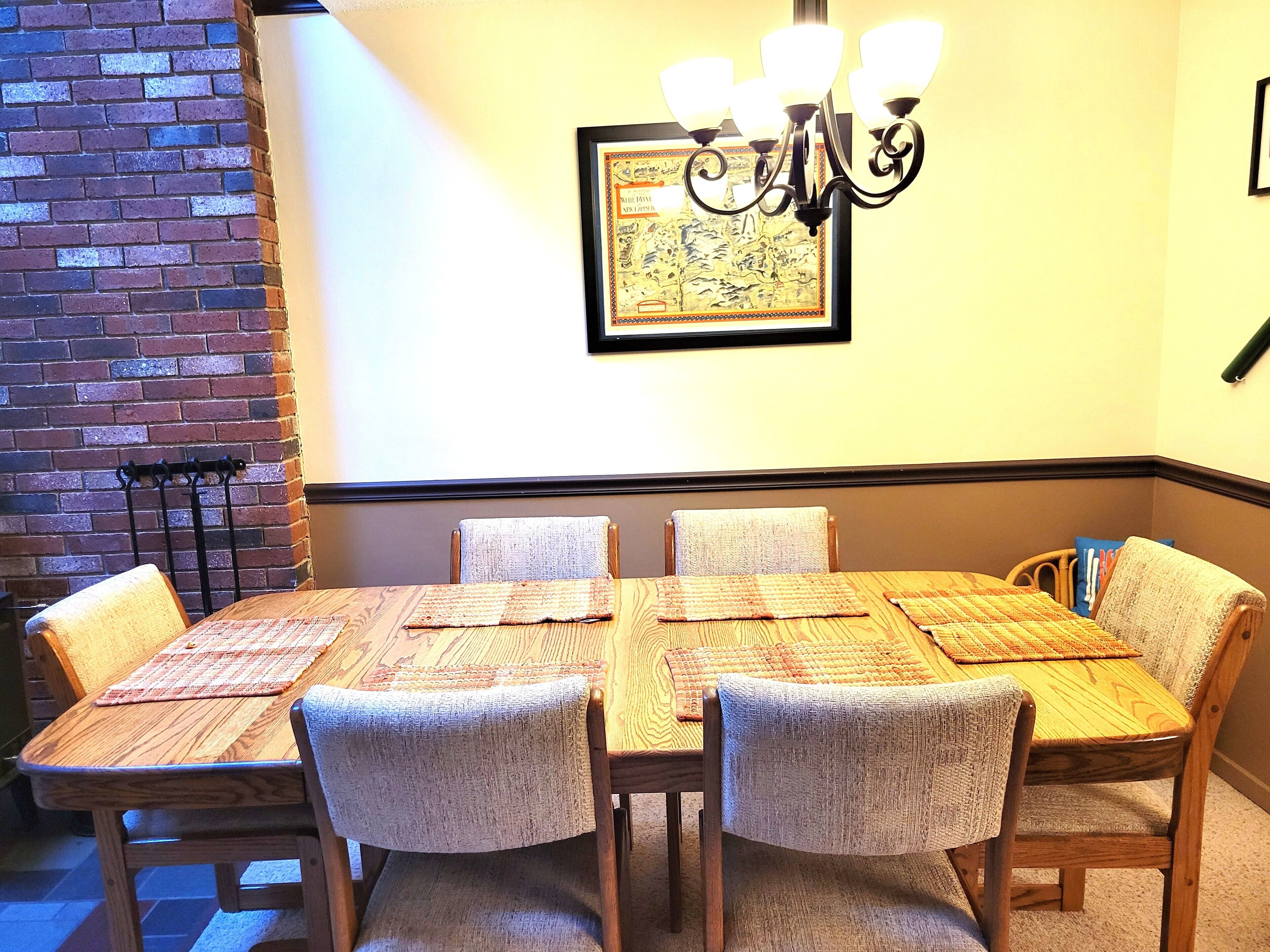 A dining area with a brick wall, a chandelier, and a framed map on the wall.