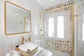 A modern bathroom with a large mirror, a white sink, a glass-enclosed shower, and a brick wall. - Borgo Veneziano by Corfuescapes (Corfu)