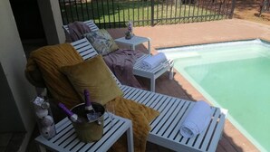 A poolside area with lounge chairs, a small table with a bottle and glass, and a metal fence in the background. - Prisatt Boutique Hotel (Lephalale)