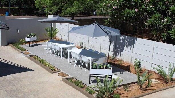 An outdoor patio with white tables and chairs, umbrellas, and small plants. - Prisatt Boutique Hotel (Lephalale)