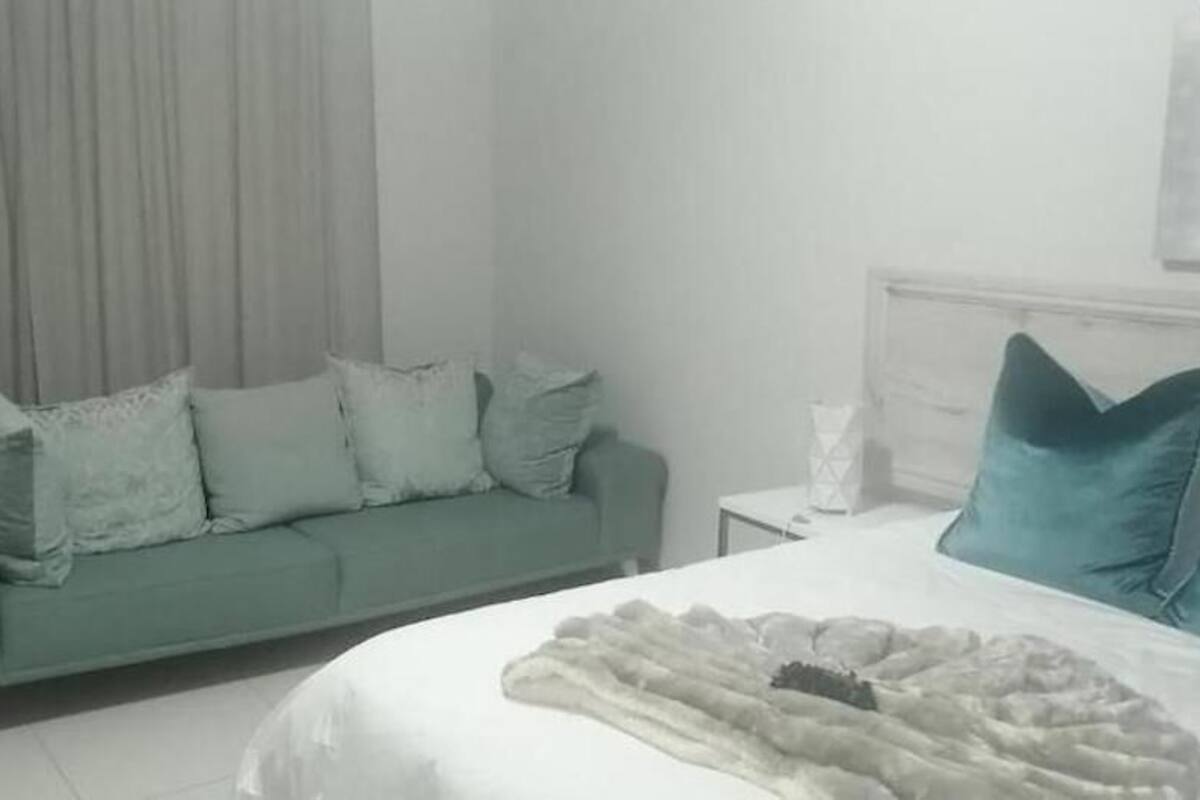 Ein Zimmer mit einem grünen Sofa, einem weißen Bett und einem Nachttisch in Weiß.