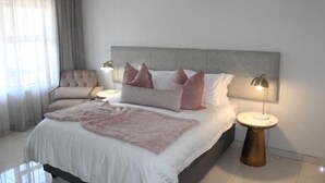 A bedroom with a bed, two bedside lamps, a bedside table, and an air conditioning unit. - Prisatt Boutique Hotel (Lephalale)